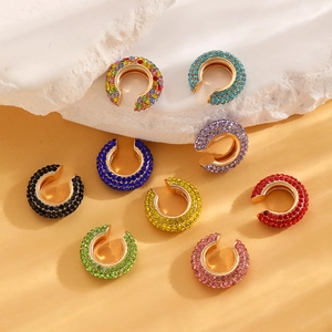 Close-up of C-shaped ear cuffs with colorful rhinestones on a textured background