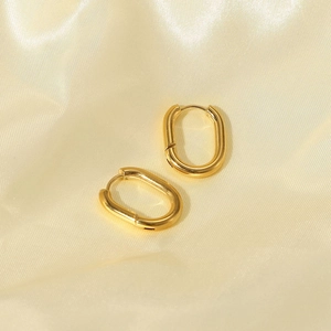 Macro shot of gold oval stainless steel hoop earrings on luxurious yellow silk fabric
