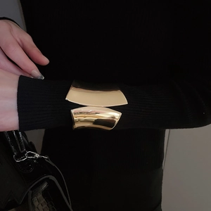 Polished gold wide open cuff bracelet worn over black knit sleeve with luxury bag