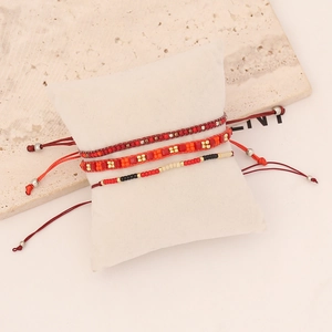 Three-piece bohemian beaded bracelet set with red and orange seed beads on a white pillow