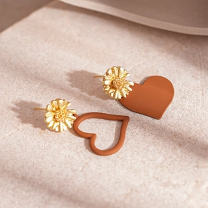 Detail view of asymmetric daisy heart earrings with matte finish on textured stone surface