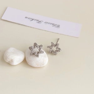 Detailed view of silver hexagonal star earrings with zircon inlay on white pebble
