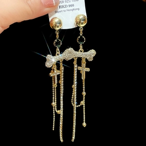 Close-up of golden bone-shaped zircon earrings with long tassels and cross charms