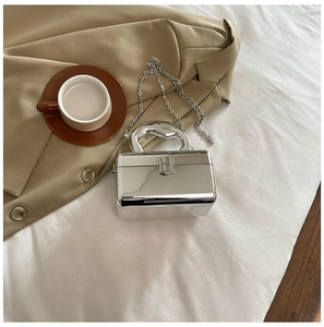 Detail of silver mirror acrylic box bag with unique top handle on a beige blazer
