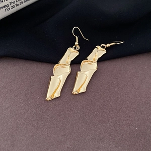 Macro detail of irregular gold geometric twisted earrings with textured metallic finish