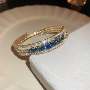 Macro shot of a layered gold bangle with blue stones and crystals on white display