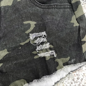 Detail der Camouflage-Denim-Shorts mit Distressed-Rissen und ausgefranstem Saum