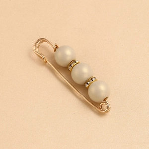 Detailed macro of gold safety pin brooch featuring three pearls and sparkling rhinestones