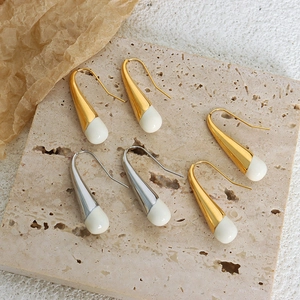 Elegant gold and silver teardrop earrings with cream drops on a textured stone surface