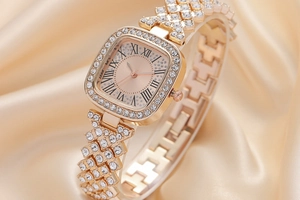 Square gold watch with rhinestones and Roman numerals on soft beige silk background