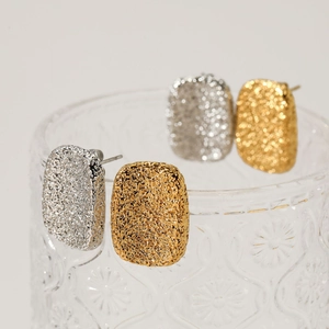 Hammered gold and silver geometric stud earrings displayed on glass with textured metal finish