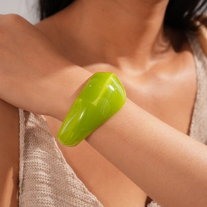 Close-up of a minimalist chunky green acrylic bangle worn on a wrist over a knit sweater