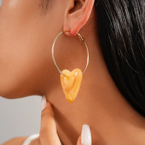 Close-up of a gold hoop earring with a marble-textured orange acrylic heart pendant