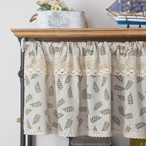 Close-up of beige linen cafe curtain with green leaf print and white lace ruffle detail