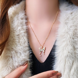 Close-up of gold butterfly pendant with sparkling zircons and green gems on a ball chain