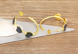 Close-up of gold C-shaped earrings with colorful heart pendants on a wooden surface