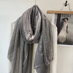 Detail of grey cotton linen scarf with elegant lace trim hanging on a wooden hanger