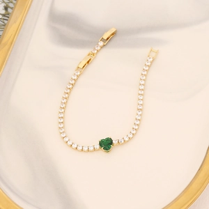 Detailed close-up of 18K gold bracelet featuring heart green zircon on marble tray