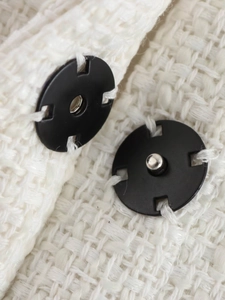 Macro view of black metal snap buttons on cream blend tweed fabric cape coat