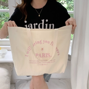 Detail of off-white canvas tote bag featuring pink floral embroidery and Paris quote