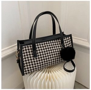 Chic houndstooth handbag with black trim and pom-pom charm on a minimalist art base