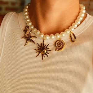 Collana di perle bianche con ciondoli marini dorati indossata da una modella con stile