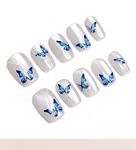 Detailed view of pearl white press-on nails with blue butterfly patterns and thin lines