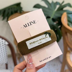 Detail of olive green ribbed scrunchie with white wildflower tag on branded card