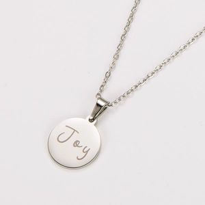 Macro detail of silver stainless steel round pendant with Joy engraving and fine chain