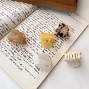 Mini-Haarklammern aus Acetat in Herzform, Schildpattbraun und Creme auf einem Buch