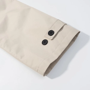 Détail du poignet de trench-coat beige avec boutons et texture en sergé de coton