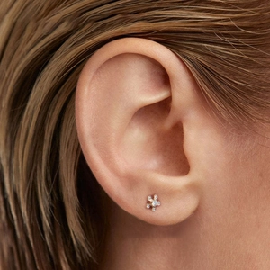 Close-up of a gold star-shaped floral earring with white zircon inlay worn by a model