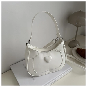 Close-up of a white crescent shoulder bag with 3D heart detail in a lifestyle setting