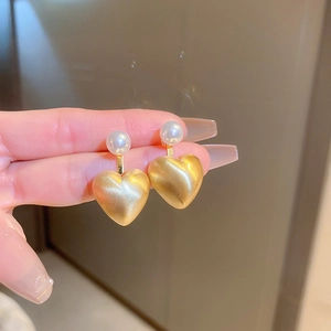 Close-up of brushed gold heart earrings with white pearls being held by hand