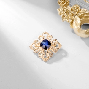Vintage gold brooch with a square blue crystal and intricate hollow swirl patterns