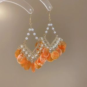 Detail of round shell pearl tassel earrings with golden hooks and orange resin discs