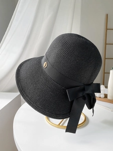 Detail of black straw sun hat featuring a grosgrain ribbon bow and gold metal accent