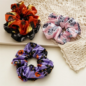 Three Halloween satin scrunchies with pumpkin, ghost, and castle prints on lace background