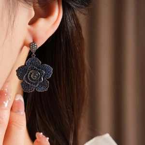 Close-up of vintage blue zircon flower earring worn on ear with dark metal detailing