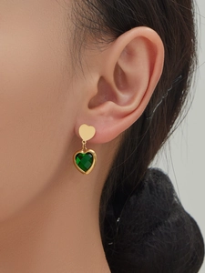 Detail of gold heart earrings with green crystal inlay worn by a model