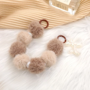 Brown and beige plush ball phone strap with iridescent bone charm on white fur