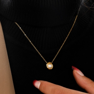Close-up of pearl pendant necklace on black turtleneck sweater showing luxury finish