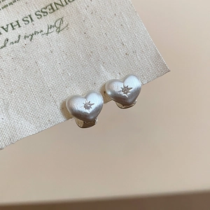 Macro shot of silver heart earrings featuring brushed metal texture and zircon center