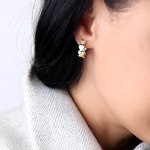 Close-up of golden heart-shaped drop earrings with inlaid diamonds worn on a model's ear