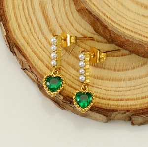 Detail of vintage gold earrings with pearls and a green heart-shaped zircon on wood