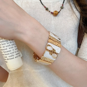 Detail of vintage gold-tone textured metal and white enamel elastic bracelet on wrist