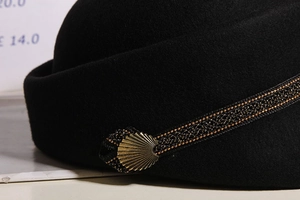 Macro detail of wool beret featuring black-gold braided strap and golden fan metal buckle