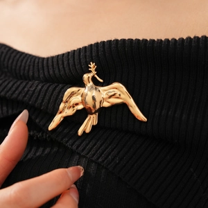 Macro detail of a polished gold bird brooch pinned on black knit fabric garment
