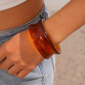 Macro detail of wide amber resin bangle with glossy finish and translucent texture