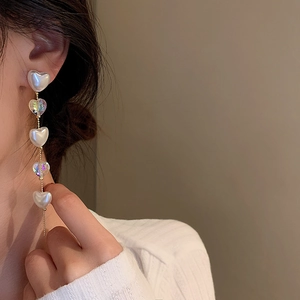 Elegant gold earrings with heart-shaped faux pearls and iridescent crystals on a model